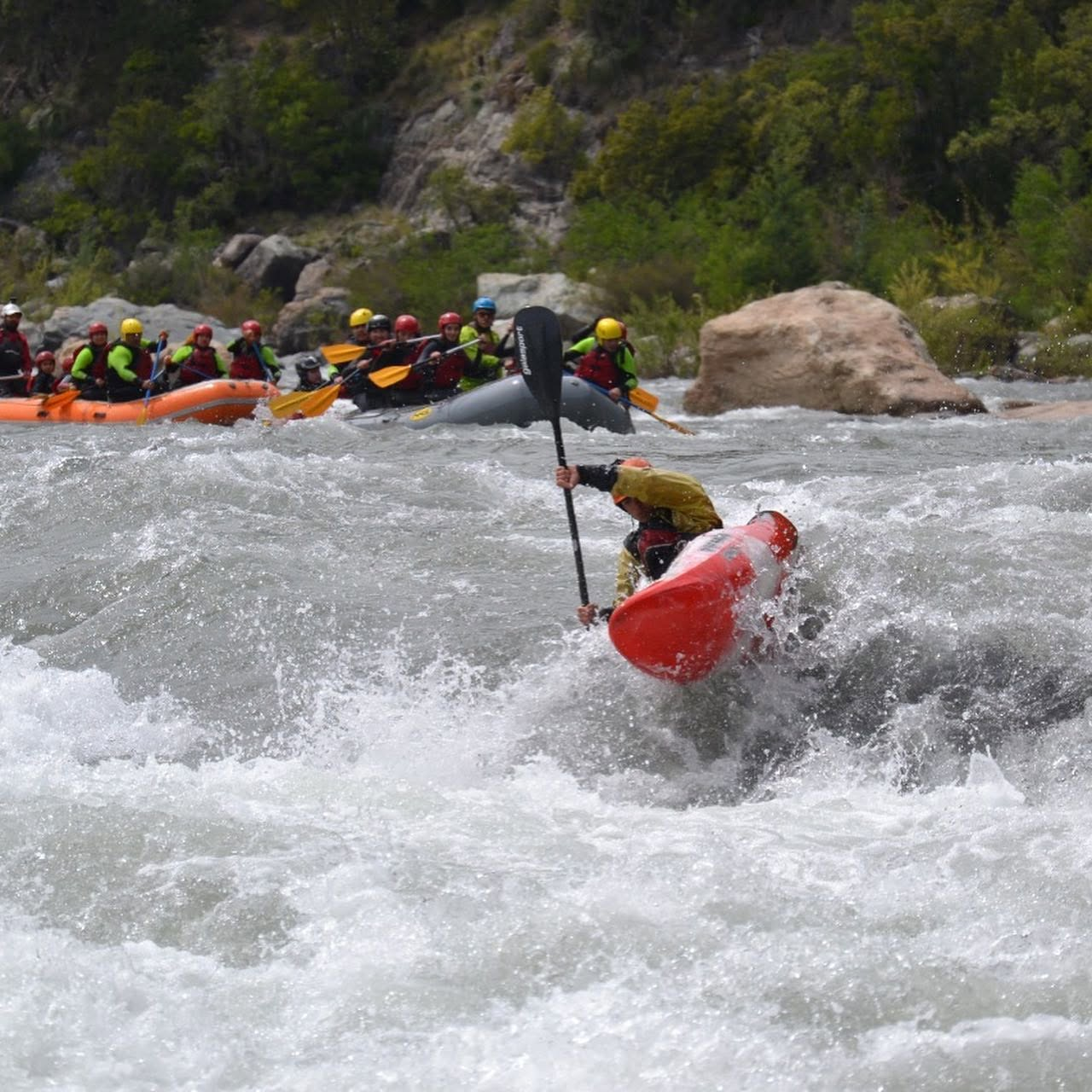 Kayak surfeando una ola con balsas de fondo